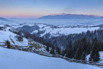 Picturesquet rural landscape with the snowy Rucar-Bran pass in the valley of Bucegi mountains at sunset, Pestera village, Brasov county, Transylvania region, Romania.