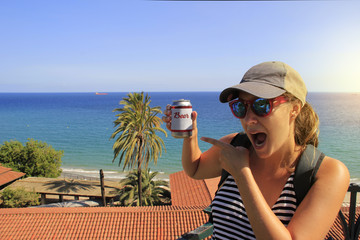 Funny tourist cap and backpack showing beer near the blue sea making jokes and pointing