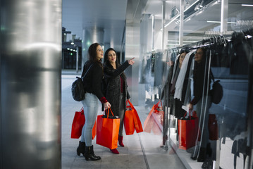 Two young women in shopping looking at shop window in the city