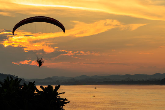 silhouette flying paramotor over river and sunset sky
