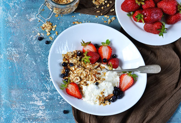 Good morning! Breakfast with yoghurt, granola and strawberries on a blue, concrete background.