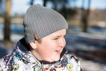 portrait of happy laughing fat kid in cap and winter jacket in park in winter