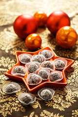 Weihnachtsbäckerei: Rumkugeln in einer roten sternförmigen Schale auf einer festlichen Tischdecke...