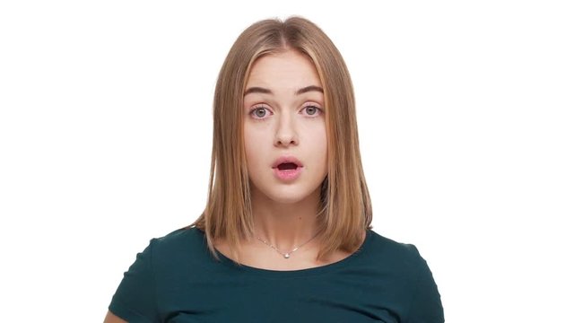 Slow motion portrait of young woman wearing green shirt being shocked raising hands close to open mouth emotionally reacting on bad news over white background. Concept of emotions