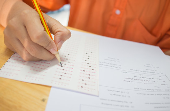 Students hands taking exams, writing examination room with holding pencil on optical form of standardized test with answers and english paper sheet on row desk chair doing final exam in classroom.