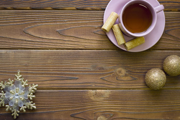 A tea cup with saucer, golden balls and a snowflake on a rustic wooden table, top view