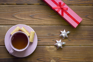 Morning surprise with a tea cup, red giftbox and shiny stars on a rustic wooden table, top view