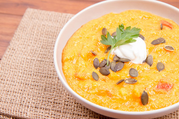 Pumpkin and carrot soup decorated with cream, parsley and pumpkin seeds on a wooden background