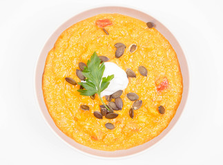 Pumpkin and carrot soup decorated with cream, parsley and pumpkin seeds on a white background