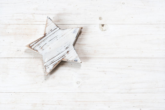 white painted wooden star on white rustic wood, christmas background or greeting card with copy space, flat top view from above