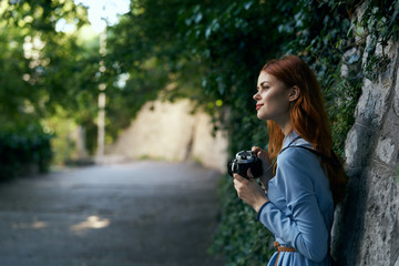 Young beautiful woman in a blue dress is holding a camera in an alley