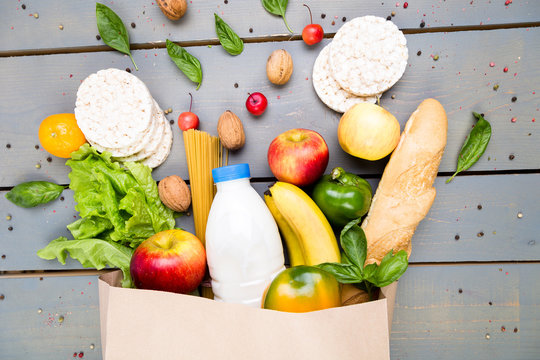 Grocery shopping concept. Different food in paper bag on wooden background.  Flat lay.