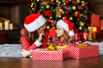 Two beautiful sisters near the christmas tree in front of the fire place having fun. love, family and happiness consept.  New year's eve. Christmas. Cozy holiday at the fir-tree 