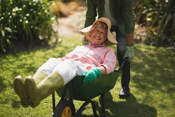 Mid section of man carrying smiling senior woman in wheel borrow