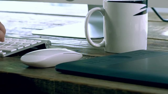 Closeup on a caucasian male freelance designer, programer working at Home typing on a wireless keyboard with electronics peripheral on the wooden table