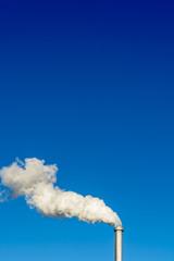 A metallic chimney giving off a heavy cloud of white smoke against a deep blue sky.