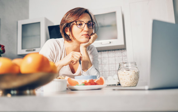 Woman prepare breakfast and watch laptop on kitchen