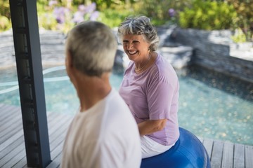 Smiling senior woman looking at man while sitting on exercise