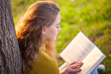 Beautiful young blonde woman sitting and reading book in a park near the lake