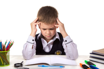 Bewildered thoughtful pupil sitting at the desk with hands over the head surrounded with stationery