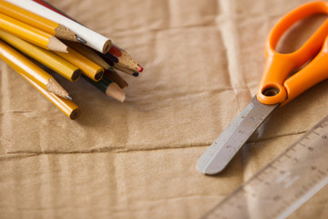 orange scissors, plastic ruler and pack of wood yellow pencils with rubber band on paperboard