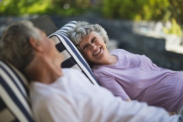 Smiling senior woman looking at man resting on lounge chair
