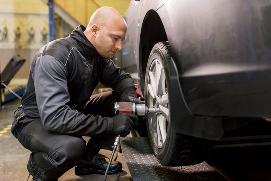 auto mechanic with screwdriver changing car tire