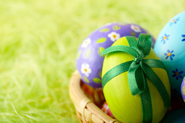 Rustic style painted easter eggs in basket on green background