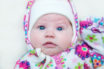 The baby is lying dressed in a warm hat and a jacket.