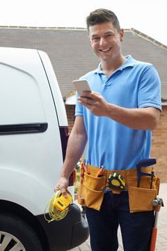 Electrician With Van Sending Text Message On Mobile Phone Outside House
