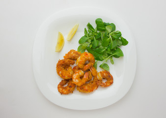 Fried shrimps on a plate. Prawns fried in breading on a white plate with salad and lemon.