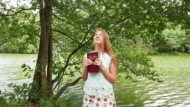 4k. Christian Bible  in hands of attractive young girl in park