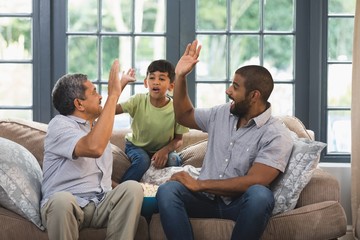 Multi-generation family giving high five while sitting together - Powered by Adobe
