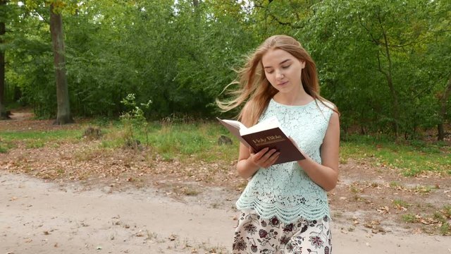 4k. Girl walks in  park and studies Bible. Steady shot