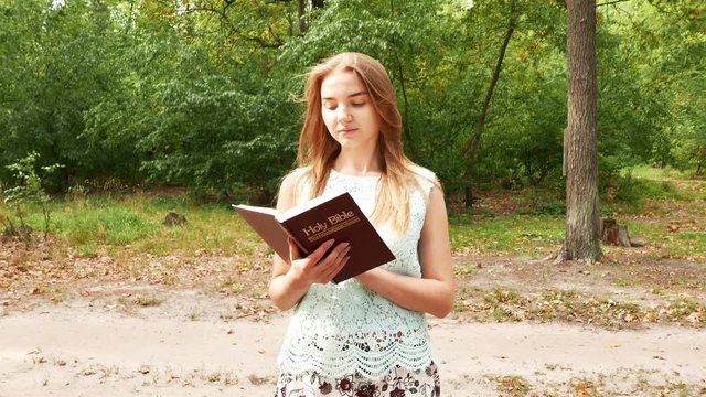 4k. Girl walks in  park and studies Bible. Steady shot