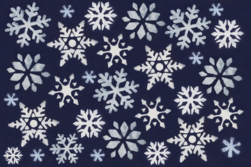 A lot of white snowflake painted with paint through a stencil on a dark blue background.