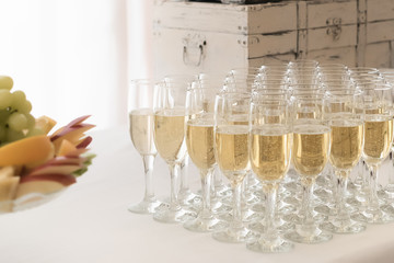 Glasses full of champagne on welcome stand with event (wedding) decorations and retro suitcase behind
