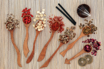 Chinese herbal medicine with herbs in wooden spoons, acupuncture needles and moxa sticks used in moxibustion therapy with feng shui coins on bamboo background. Top view.