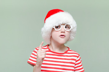 Disgruntled boy in Santa's hat and glasses threatens with a finger