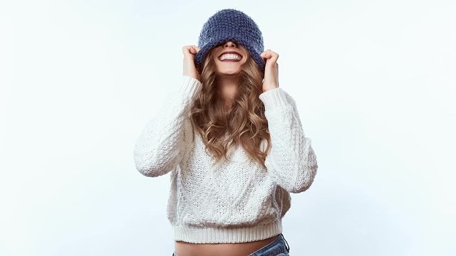 Portrait of sensual positive beautiful blond woman in sweater and blue hat isolated on white background in studio