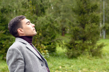 Portrait of young attractive man with a grey coat, breathing in the fresh autumn air in the Park, showing his face to the wind. The concept of freedom, ecology, life without borders