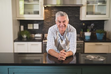 Smiling senior man leaning on kitchen counter at home