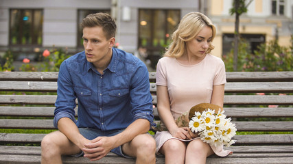 Unhappy couple sitting after fight, girl with flowers, problem in relationship