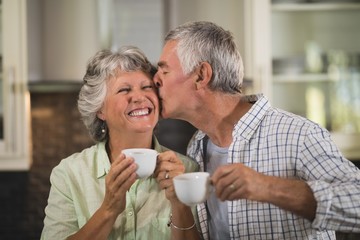 Fototapeta na wymiar Senior man kissing wife while having coffee