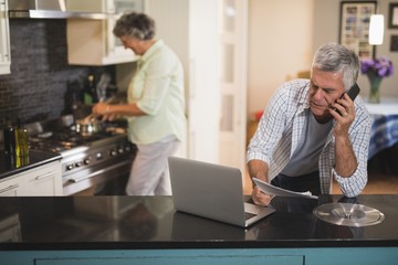 Senior man talking on phone while woman cooking in kitchen