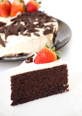 Chocolate cake decorate with whipping cream, sliced chocolate and fresh strawberries. On white plate over white background. Sweet dessert for celebrate.