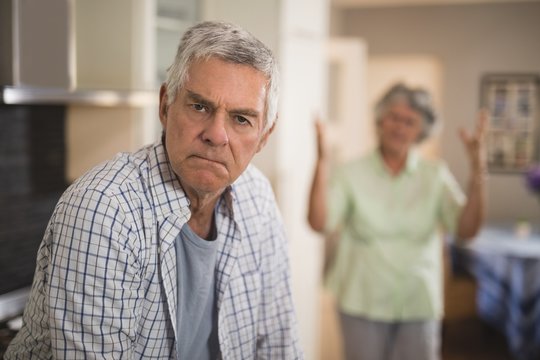 Portrait of unsmiling senior man with angry woman in background