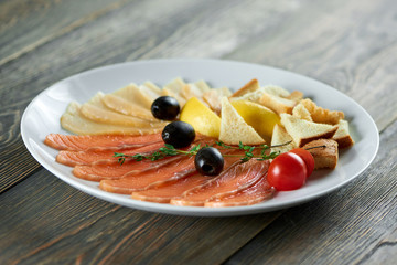 Shot of a plate with sliced smoked salmon black olives and cherry tomatoes served with sliced lemons on wooden table eating food appetizer restaurant food eating dish concept.