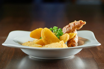 Shot of a plate with grilled sliced potatoes and chicken sausage served on a wooden table at the restaurant eating nutrition meat unhealthy calories meal supper dinner lunch.