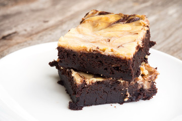 Cheese brownies on white plate. Homemade dessert for chocolate lover. Served on wooden table.